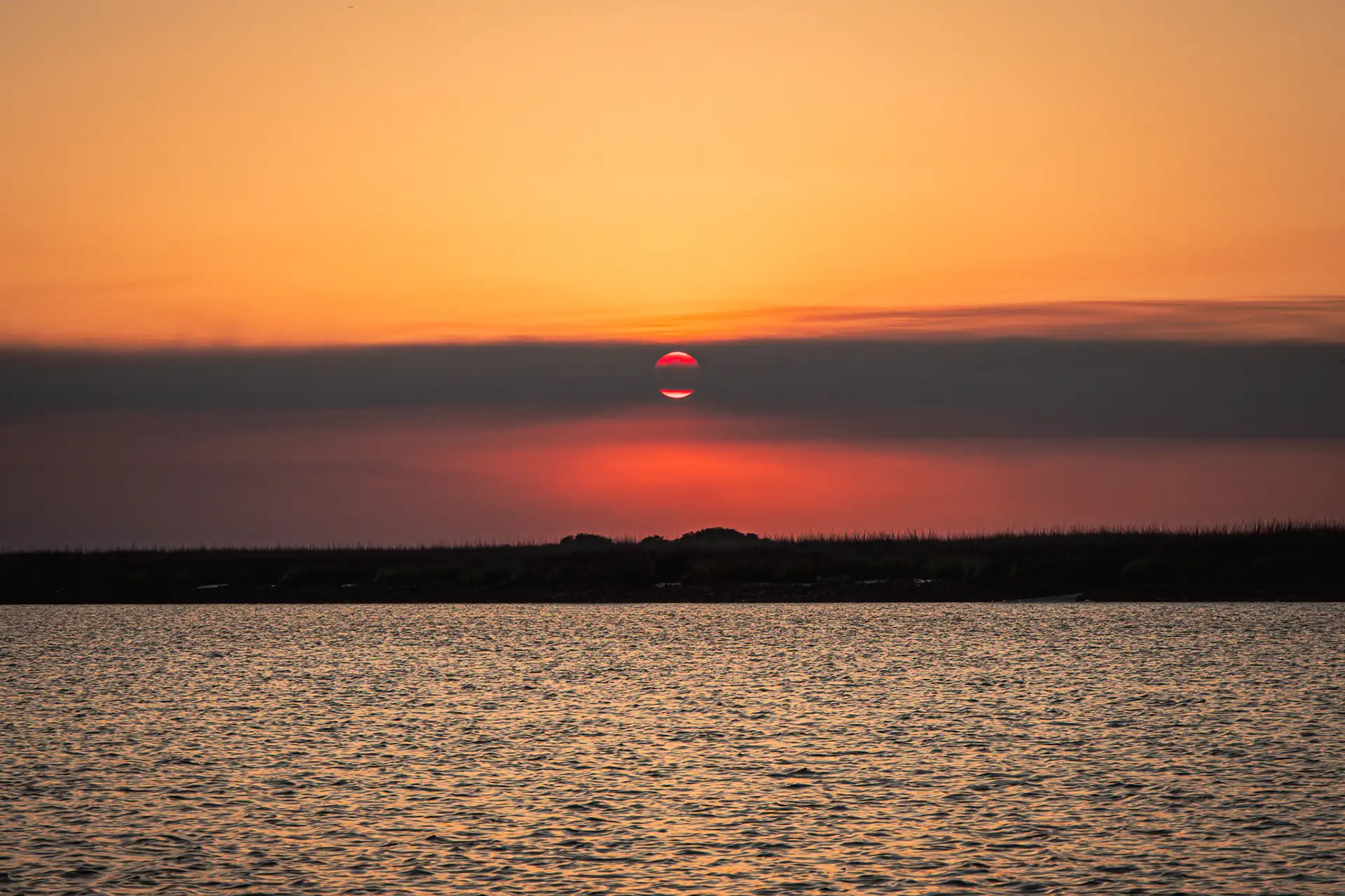 A stunning sunset over St. Catherines Island. A cloud perfectly bisects horizontally the red sun.
